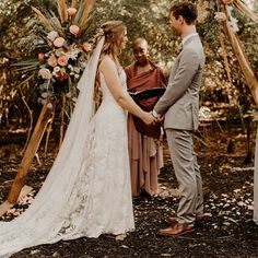 a bride and groom holding hands during their wedding ceremony in the woods with an arch decorated with flowers