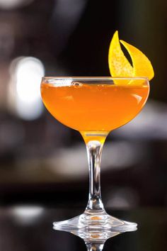 a close up of a drink in a wine glass with an orange peel on the rim