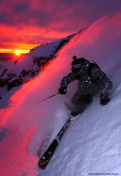 a man riding skis down the side of a snow covered slope at sunset or dawn