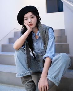 a woman sitting on the steps with her hand under her chin and wearing a hat