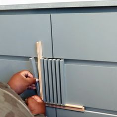 a person holding a piece of wood in front of a gray cabinet with drawers on it