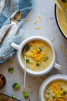 two bowls of broccoli cheese soup on a table with spoons and napkin