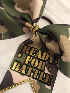 the ready for battle tag is attached to a camo - colored bow with gold sequins