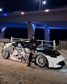 a woman sitting on the hood of a sports car in front of a bridge at night