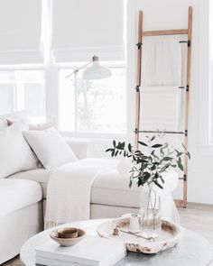 a living room with white couches and pillows on the table in front of a window