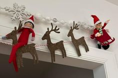 two elfs are hanging on the mantle next to some reindeer decorations and one is wearing an elf's hat