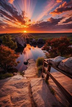 the sun is setting over a river with rocks and trees on either side, as well as a wooden bench