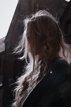 a woman with long hair standing in front of a building and looking off into the distance