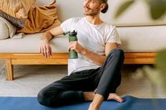 a man is sitting on the floor with his yoga mat and holding a water bottle