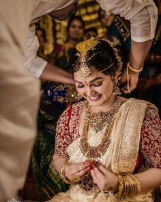 a woman in a red and gold bridal outfit looking at her cell phone while she is getting ready to get married