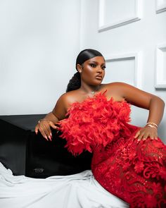 a woman in a red dress sitting on a bed with her hands on her hips