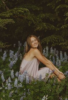 a beautiful woman sitting in the middle of blue flowers with her hands on her hips