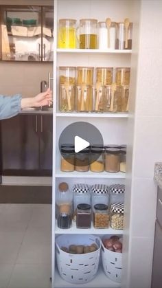 a woman standing in front of a kitchen counter with lots of food on shelves next to her