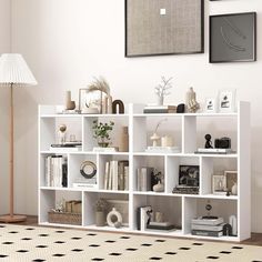 a white book shelf filled with books next to a lamp and pictures on the wall