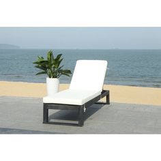 a white lounge chair sitting on top of a cement floor next to the ocean with a potted plant in front of it