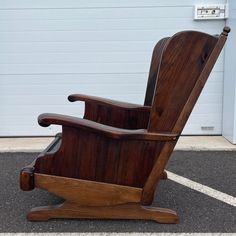 a wooden rocking chair sitting on top of a parking lot next to a garage door