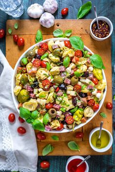 a salad with tomatoes, olives and other ingredients on a wooden cutting board next to some condiments