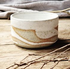 a white and brown bowl sitting on top of a wooden table next to dry twigs