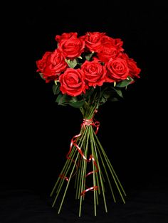 a bouquet of red roses on a black background with ribbon and bow tied around the stems