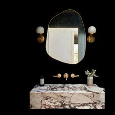 a bathroom vanity with marble counter top and gold faucet, along with two wall lights