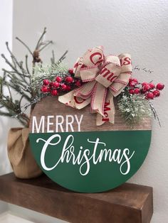 a merry christmas sign on top of a wooden shelf with greenery and bows around it