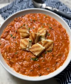 a white bowl filled with red sauce and croutons on top of it next to a spoon