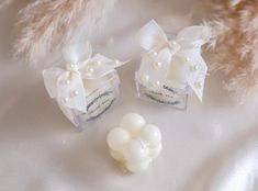 two small boxes with pearls on them sitting on a white surface next to some feathers