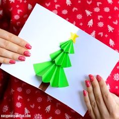 a woman holding a paper christmas tree on top of a white card with green origami