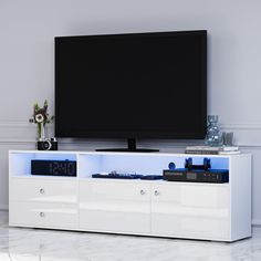 a flat screen tv sitting on top of a white entertainment center next to a vase with flowers