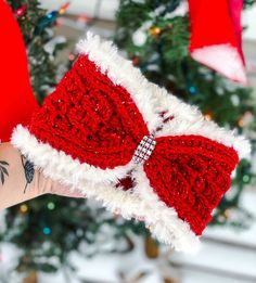 a hand holding up a red and white knitted christmas stocking with a bow on it