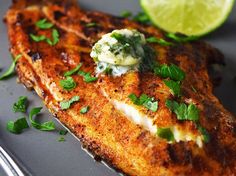 a piece of fish is on a plate next to a fork and lemon wedges