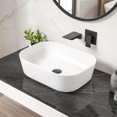 a white sink sitting on top of a black counter next to a mirror and plant