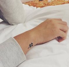 a person's hand with a small tattoo on their left wrist, resting on a bed