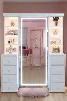 an open closet with white drawers and lights on the doors, in front of a pink wall