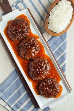 three meatballs covered in sauce on a white plate with chopsticks next to it