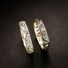 two wedding rings sitting next to each other on a black surface in front of a dark background