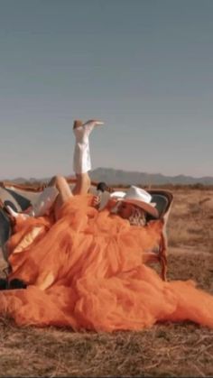 a woman laying on top of an orange blanket in the middle of a dry grass field