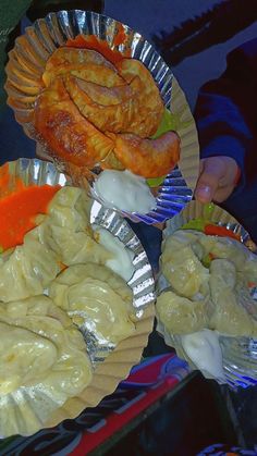 some food is sitting on tin foil plates and being held by someone's hand