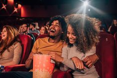 two people sitting in a movie theater with popcorn buckets