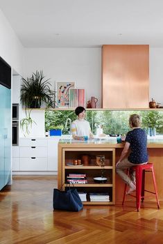 two women sitting at a kitchen island in the middle of a wooden floored room