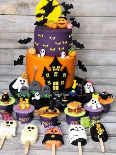 a halloween themed cake surrounded by cupcakes and candy sticks on a wooden table