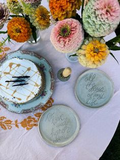 a table topped with plates and flowers on top of a white table cloth covered in writing