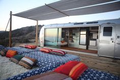 an airstream is set up on the deck with lots of pillows and blankets to sit on