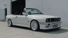 a white bmw convertible parked in front of a building with its doors open and the roof down