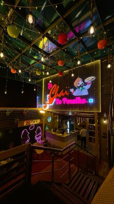 the inside of a restaurant with neon lights and decorations on the ceiling, along with people walking down the stairs