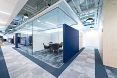 an empty office with glass walls and blue partitions on the wall, along with tables and chairs