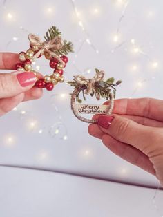 two hands holding christmas ornaments with lights in the background