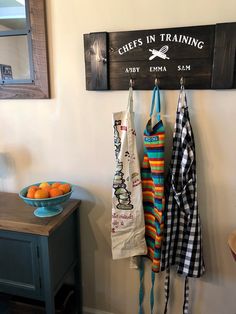 three aprons hanging on a wall next to a bowl of oranges and a sign that says chefs in training