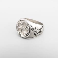 a silver ring with flowers on it and chinese characters in the middle, sitting on a white surface