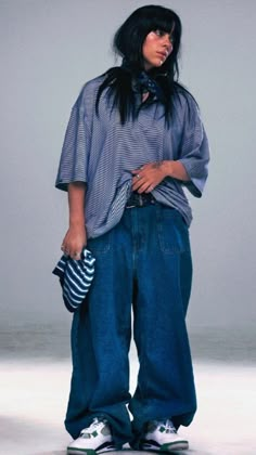 a woman with black hair wearing blue jeans and a striped shirt is standing on a skateboard